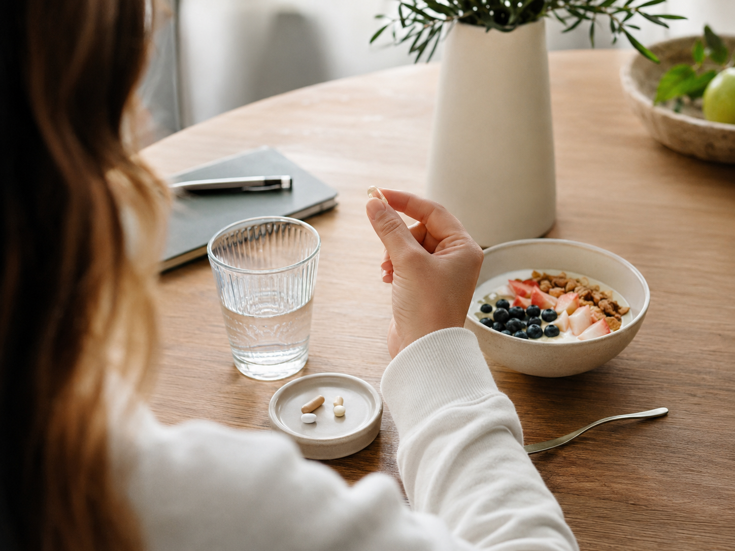 Person integriert ihre Vitaminroutine entspannt in den Morgen am Frühstückstisch.